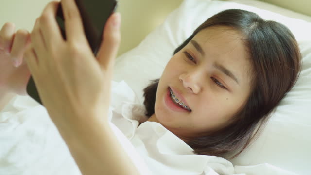 Junge-asiatische-Frau-aufwachen-am-Morgen-und-mit-dem-Smartphone-auf-dem-Schlafzimmer.
