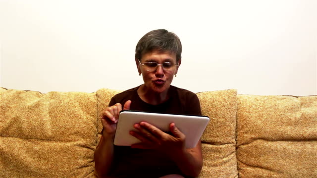 Eine-attraktive-erwachsene-Frau-ist-Video-Chat-mit-ihrer-Familie,-auf-einem-Tablet-PC,-sitzen-auf-einem-Sofa-zu-Hause.