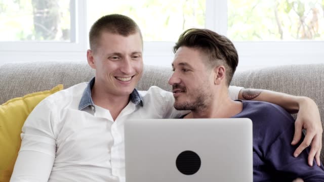 Pareja-gay-relajándose-en-el-sofá-usando-la-computadora-portátil.-Navegando-por-Internet.