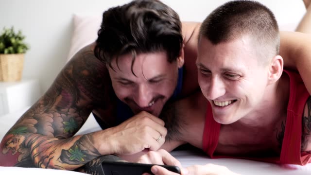 Gay-couple-in-bed-using-phone.-Browsing-internet.