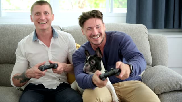Gay-couple-relaxing-on-couch-with-dog-playing-games.-Dog-is-confuse.
