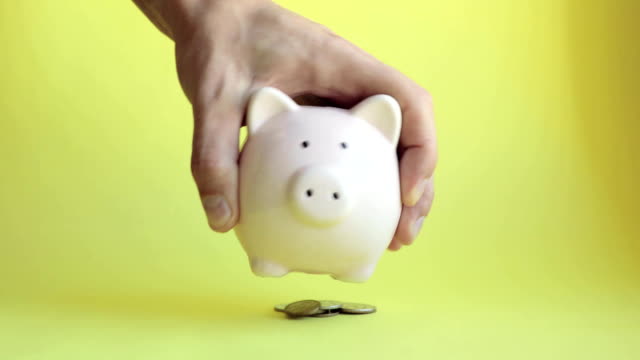 Mann-schüttelt-Sparschwein-von-Schweineform-und-Münzen-fallen-auf-gelbem-Hintergrund
