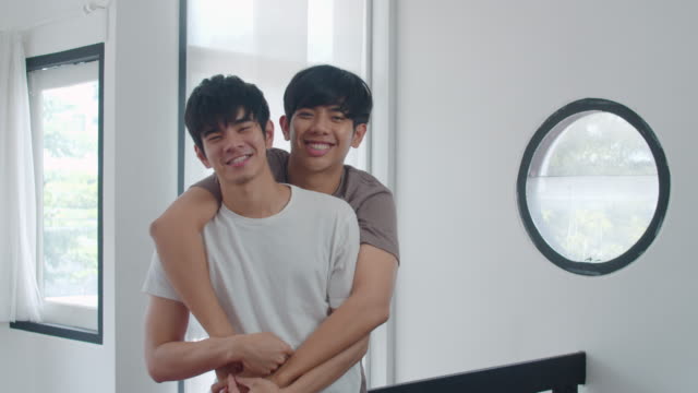 Porträt-Junge-asiatische-Homosexuell-Paar-gefühl-glücklich-lächeln-zu-Hause.-Asiatische-LGBTQ-Männer-entspannen-zu-schüchtern-Lächeln-blickend,-während-Umarmung-im-Wohnzimmer-zu-Hause-im-MorgenKonzept.