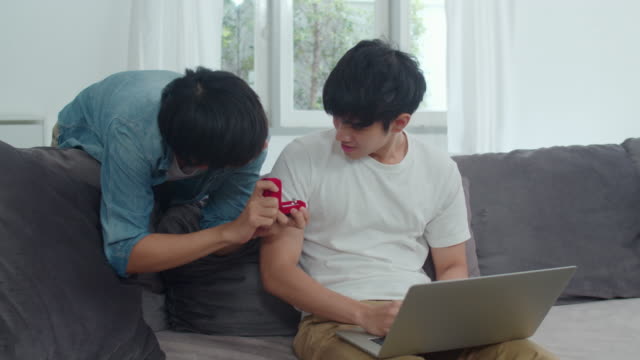 Young-Asian-gay-couple-propose-at-modern-home,-Teen-korean-LGBTQ-men-happy-smiling-have-romantic-time-while-proposing-and-marriage-surprise-wear-wedding-ring-in-living-room-at-house-concept.