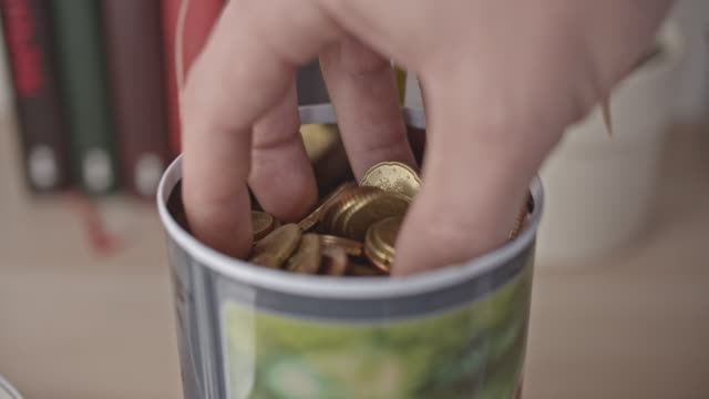 Male-hand-takes-a-handful-of-euro-coins-and-bank-note-from-a-jar