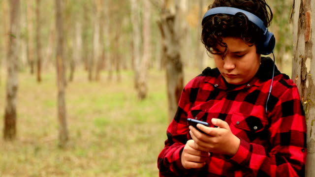 Teenage-boy-with-headphone-using-smartphone-at-the-nature