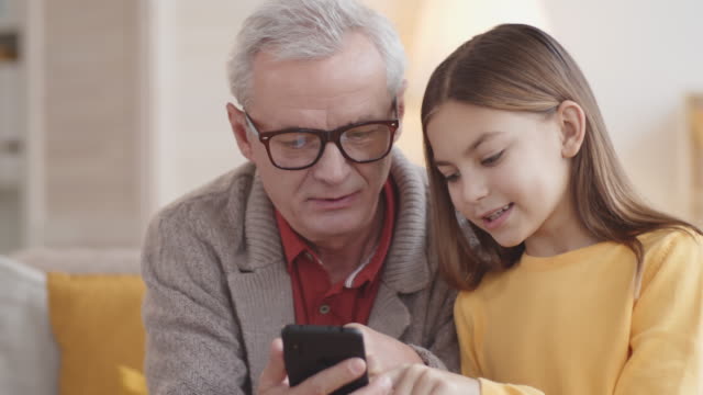 Chica-caucásica-de-10-años-enseñando-abuelo-cómo-usar-el-teléfono-inteligente