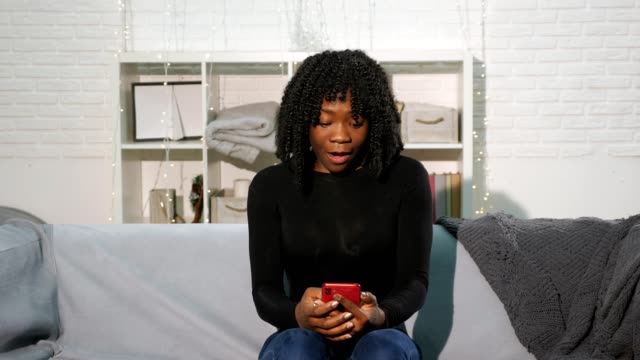 African-American-girl-looks-at-smartphone-and-becomes-happy