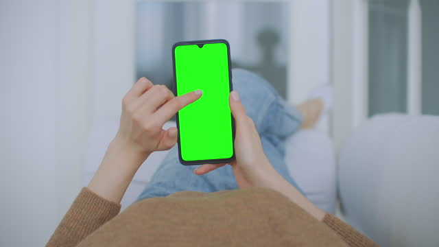 Point-of-View-of-Woman-at-Modern-Room-Sitting-on-a-Chair-Using-Phone-With-Green-Mock-up-Screen-Chroma-Key-Surfing-Internet-Watching-Content-Videos-Blogs-Tapping-on-Center-Screen