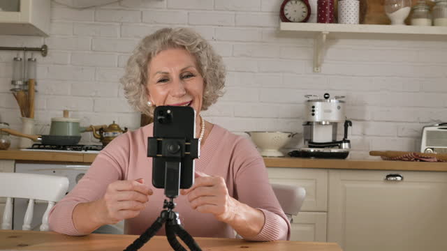 Pensioner-blogger-speaks-at-smartphone-on-tripod-in-kitchen