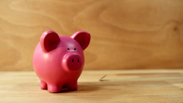 Coins-falling-into-piggy-bank-against-wooden-background