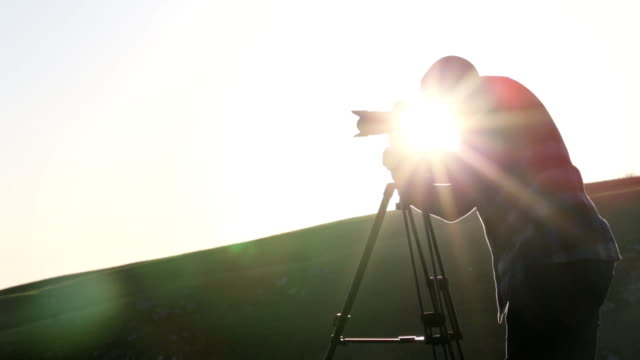 Der-Fotograf-Aufnahmen-mit-Kamera-und-Stativ-auf-dem-Hügel.