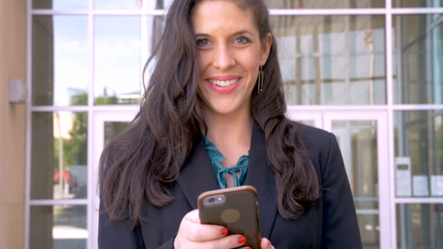 A-female-corporate-executive-looks-up-from-her-mobile-device-and-smiles
