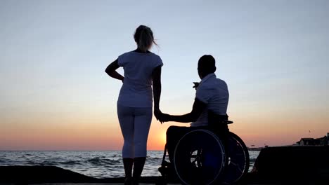 Couple-looking-into-distance,-disabled-man-in-wheelchair-and-woman-evening