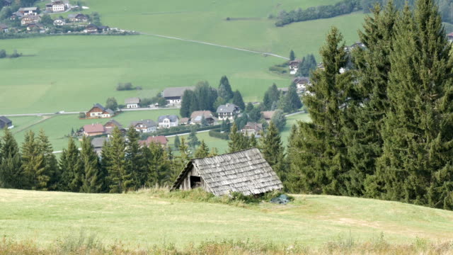 Cozy-very-old-vintage-wooden-house-in-the-Austrian-Alps-on-a-hill-with-green-grass-on-the-background-of-new-modern-houses,-Old-rural-country-wooden-house-in-village