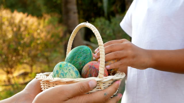 Close-up-of-woman-hand-holding-a-basket-with-easter-eggs.-Children-put-eggs-into-basket-in-sunshine-background