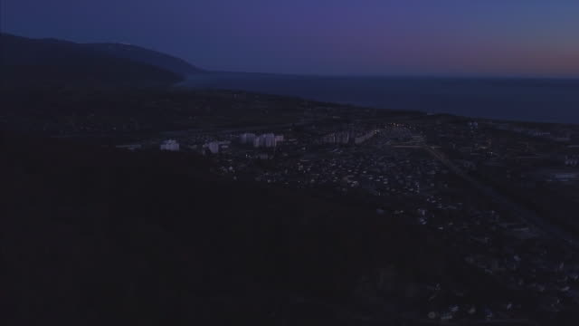 Night-panorama-of-the-city-of-Sochi-from-a-bird's-eye-view.-Clip.-Panorama-of-Sochi-from-the-air.-Houses,-streets,-trees,-the-night-sky-are-visible.-In-the-distance-you-can-see-the-sea.-Sochi,-Russia