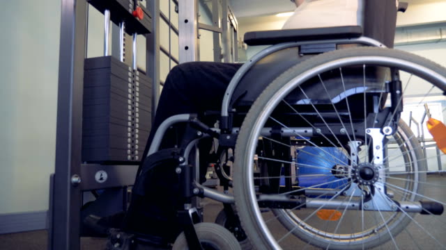 Vista-lateral-de-un-hombre-discapacitado,-levantamiento-de-pesas-en-un-gimnasio-mientras-estaba-sentado-en-una-silla-de-ruedas