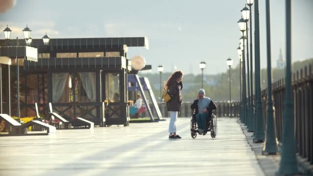 Hombre-discapacitado-en-silla-de-ruedas-hablar-por-teléfono,-caminar-juntos-a-su-novia-en-el-muelle