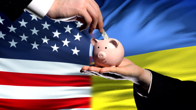 US-investment-in-Ukraine,-hand-putting-money-in-piggybank-on-flag-background