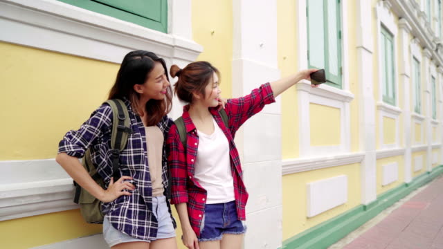 Traveler-backpacker-Asian-women-lesbian-lgbt-couple-travel-in-Bangkok,-Thailand.-Happy-blogger-young-female-couple-using-smartphone-for-selfie.