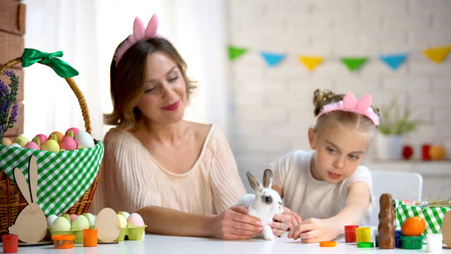 Little-girl-playing-with-cute-small-rabbit-in-mothers-hands,-pet,-Easter-symbol