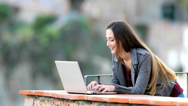 Feliz-mujer-escribiendo-en-un-ordenador-portátil-en-un-balcón