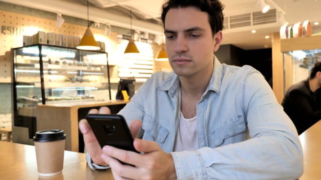 Young-Man-Typing-Message-in-Cafe,-Browsing-on-Phone