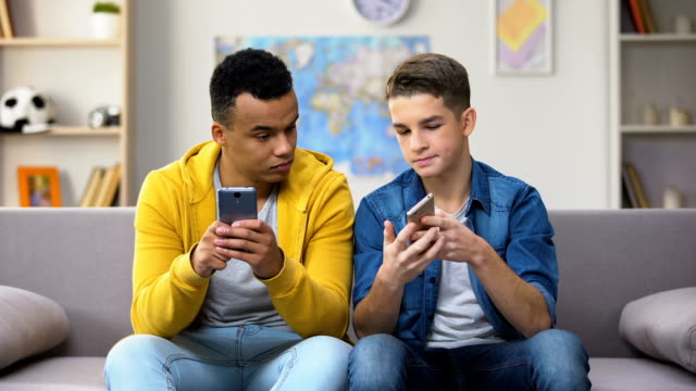 Adolescentes-afroamericanos-y-caucásicos-jugando-juegos-en-los-teléfonos,-mostrando-resultados