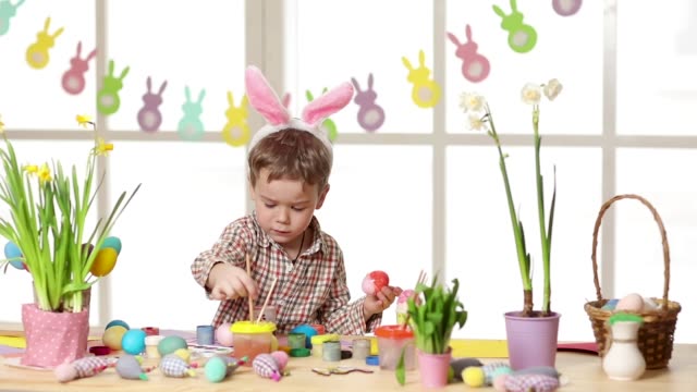 Happy-child-wearing-bunny-ears-painting-eggs-on-Easter-day.