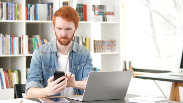 Casual-Redhead-Man-Using-Phone-and-Laptop