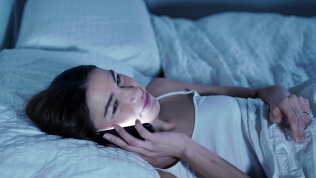 Una-mujer-en-su-cama-y-utiliza-su-teléfono-para-enviar-mensajes-remotamente,-VideoCall-y-aparecen-gráficos-futuristas.