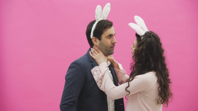 Young-couple-standing-standing-on-pink-background.-During-this,-they-carry-out-the-movement-of-rabbits.-The-woman-put-her-hands-on-his-neck,-choking.-After-this,-you-are-genuinely-laughing.