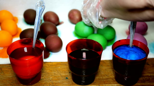 Woman-paints-Easter-eggs-in-different-colors,-dipping-them-into-cups-with-multicolored-dyes.