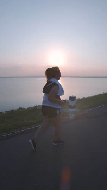 Vertikale-Videos.-Asiatische-Frauen-joggen-in-der-Straße-am-frühen-Morgen-Sonnenlicht-am-Wasserspeicher-Pa-Sak-Jolasid-Dam.-Konzept-des-Gewichtsverlustes-mit-Bewegung-für-die-Gesundheit.-Langsame-Bewegung,-Rückansicht