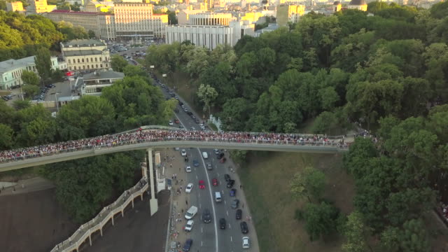 A-crowd-of-people-on-a-pedestrian-bridge-in-the-spring-evening.-Aerial-view.-A-new-bicycle-pedestrian-bridge-in-the-center-of-the-capital-of-Ukraine,-the-city-of-Kiev.-Excursions-and-walks-for-tourist