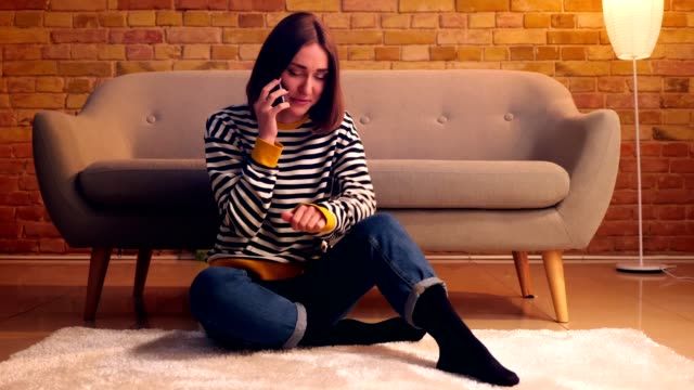 Closeup-portrait-of-young-pretty-girl-having-a-conversation-on-the-phone-and-talking-casually-sitting-on-the-floor-in-a-cozy-apartment-indoors