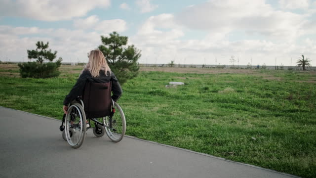 Glückliche-junge-Frau-wirbelt-ihren-Körper-im-Rollstuhl-im-Parkbereich-an-sonnigen-Tagen