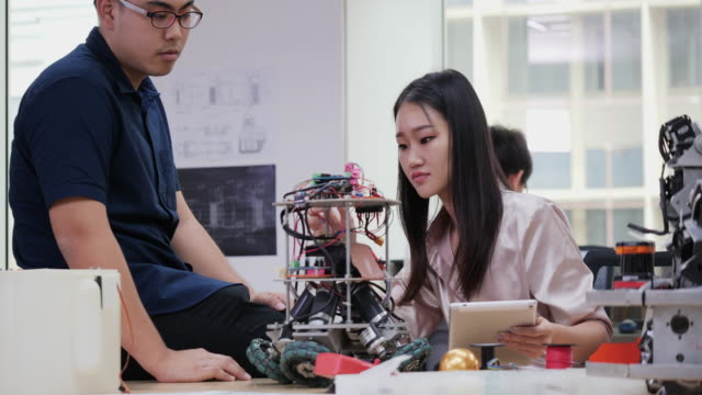 Female-electronics-engineer-working-with-robot-project-at-lab-with-friend.-Technology-and-innovation-concept.