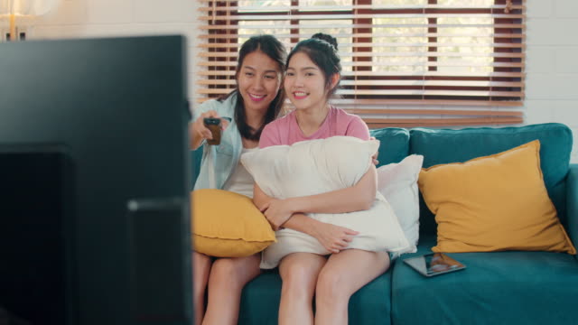 Joven-pareja-lesbiana-asiática-viendo-la-televisión-juntos-mientras-se-acuesta-sofá-en-la-sala-de-estar-en-casa.