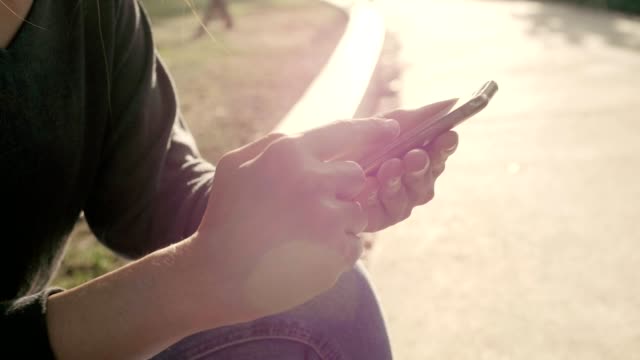Mujer-usar-el-teléfono-móvil-y-sentarse-en-el-parque-con-efecto-de-luz-solar