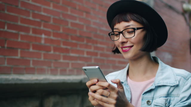 Slow-motion-of-joyful-woman-using-modern-smartphone-walking-outdoors-in-city