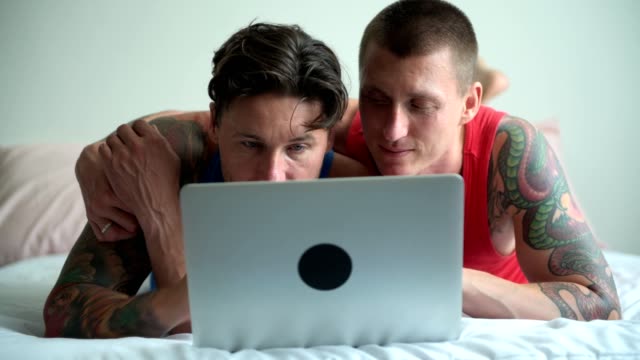 Schwules-Paar-im-Bett-mit-Laptop-Computer.-Tippen-und-Betrachten-des-Bildschirms.