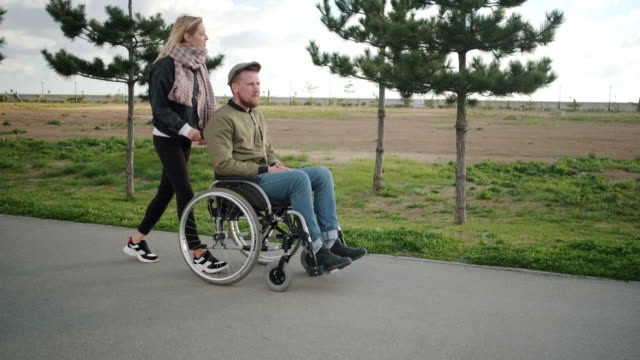 Young-woman-walking-with-handicapped-man-in-wheelchair
