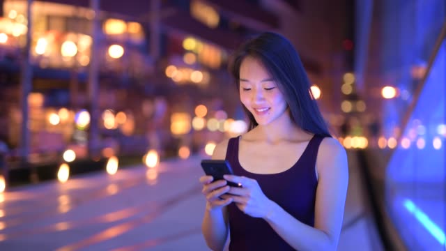 Glückliche-junge-schöne-asiatische-Frau-mit-Telefon-in-der-Stadt-in-der-Nacht