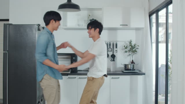 Asiatische-Homosexuell-Paar-tanzen-zu-Hause.-Junge-asiatische-LGBTQ-Männer-fühlen-sich-glücklich-Spaß-tanzen,-singen,-Musik-hören,-während-in-der-Küche-zu-Hause-Konzept.-Zeitlupe-Schuss.