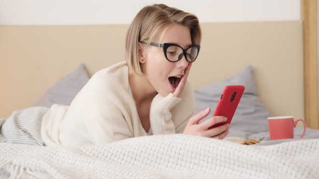 Schockierte-junge-Frau,-die-auf-Handy-im-Bett-schaut