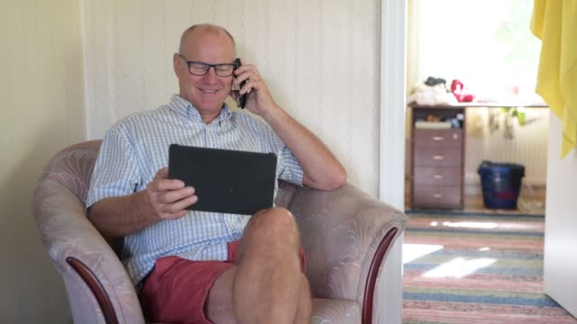 Glücklicher-Senior-Mann-mit-digitalen-Tablet-und-Telefon-zu-Hause