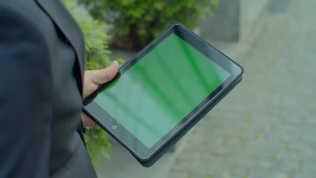 Overhead-view-businessman-browsing-internet-online-on-digital-tablet-outdoors.-Close-up-business-man-working-on-touchpad-on-street.-Male-hands-typing-on-pad-with-green-screen-in-slow-motion.