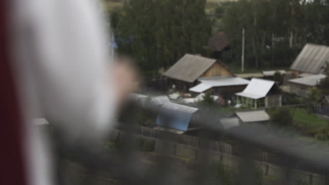 Rear-view-of-a-woman-in-white-clothes-at-the-balcony.-Stock-footage.-Close-up-of-tender-hand-of-a-female-touching-iron-handrail-of-the-balcony-on-blurred-background.